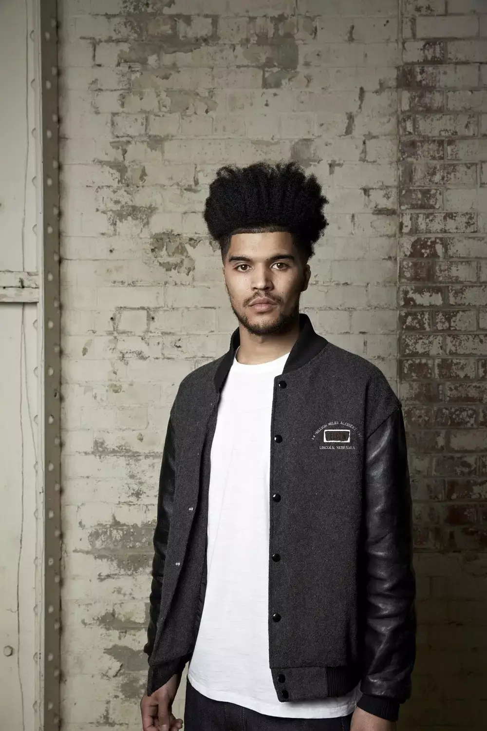 Man with high top afro with beard and white shirt and grey jacket