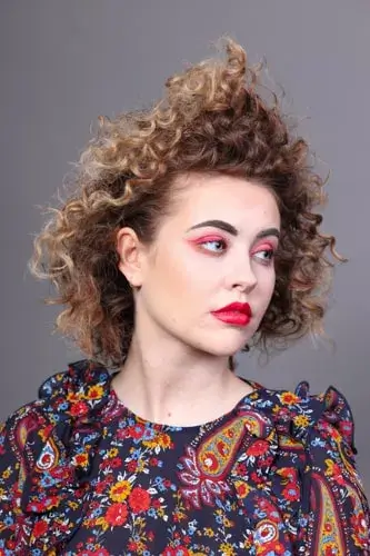 Woman with curly caramel blonde hair in red lipstick and patterned shirt